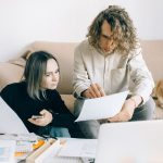 書類を見ながら相談する男女と、そばでくつろぐコーギー
